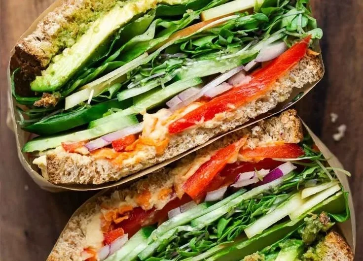 A colorful veggie sandwich filled with fresh vegetables and herbs.