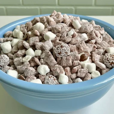 Bowl of Hot Chocolate Puppy Chow with chocolate drizzles and marshmallows