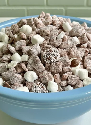 Bowl of Hot Chocolate Puppy Chow with chocolate drizzles and marshmallows