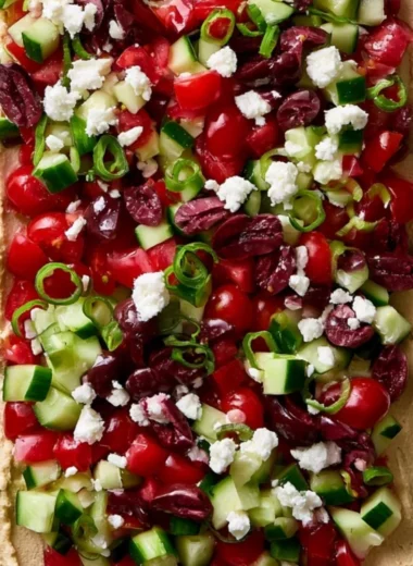 Delicious layered Greek dip with vegetables and feta cheese in a serving dish