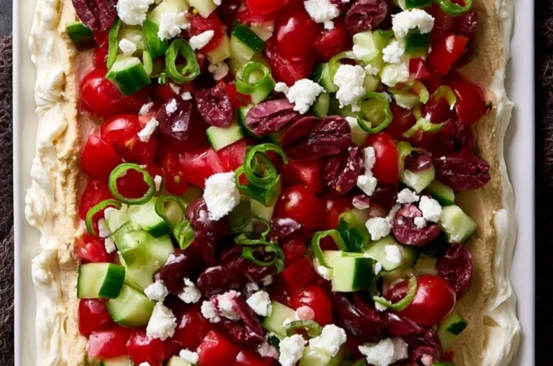 Delicious layered Greek dip with vegetables and feta cheese in a serving dish
