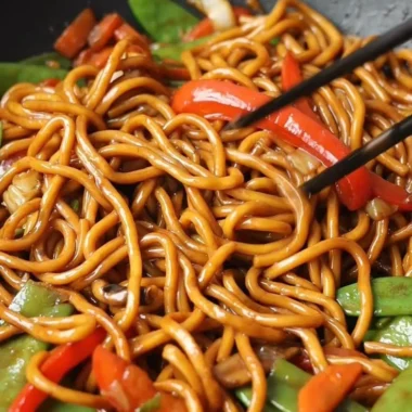 A bowl of Lo Mein noodles topped with colorful vegetables and savory sauce.