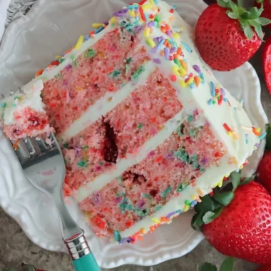 A vibrant Strawberry Funfetti Cake decorated with colorful sprinkles and fresh strawberries.