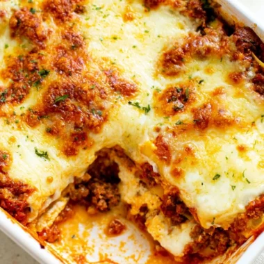 Cozy Easy Lasagna topped with melted cheese and fresh herbs on a baking dish.
