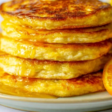 Cozy orange ricotta pancakes served on a plate, drizzled with syrup.