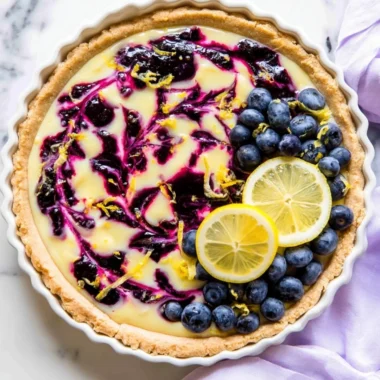 Creamy lemon tart topped with blueberry sauce on a white plate