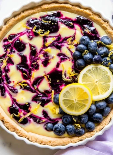 Creamy lemon tart topped with blueberry sauce on a white plate