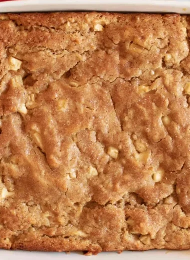 Slice of homemade Amish Apple Cake with apples and cinnamon on a wooden table